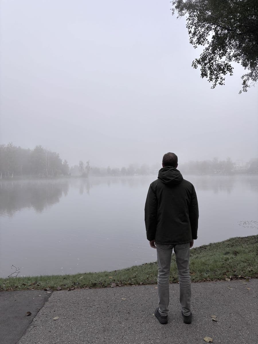 Someone standing at the edge of a lake on a foggy evening.
