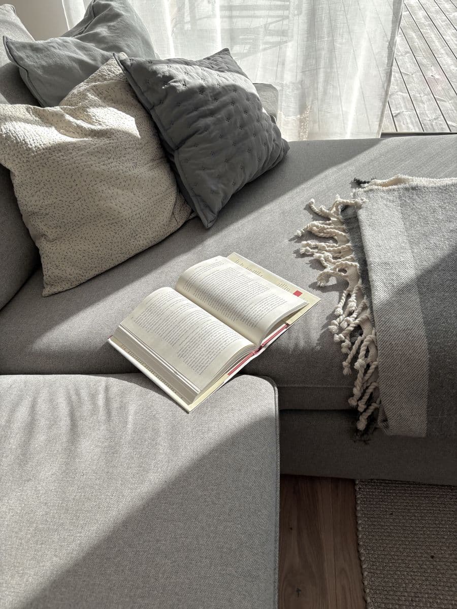 An open book on a grey sofa in late-morning light.